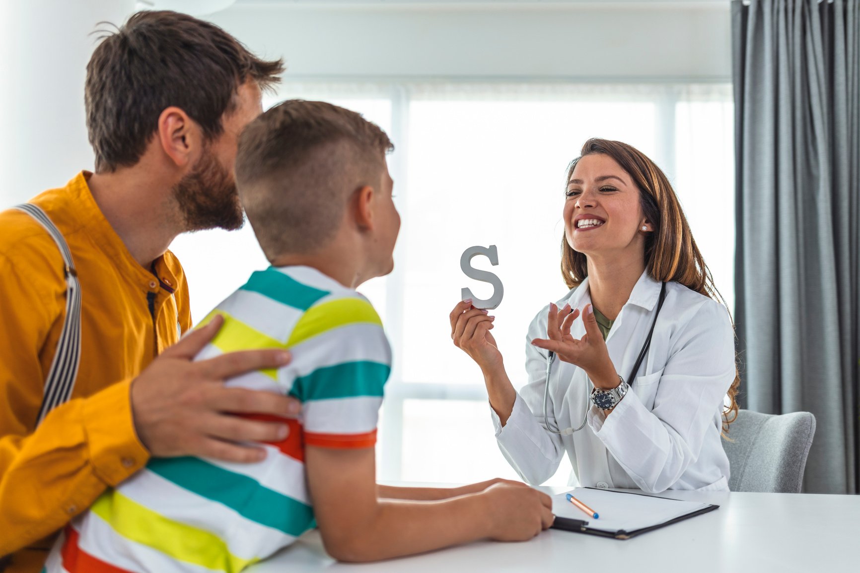 Female therapist helping boyl in speech therapy exercise